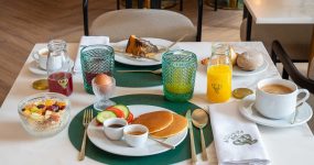 Table set for breakfast with pancakes, fruit salad, juice, coffee, bread rolls, croissant and a green placemat centerpiece on a marble table.