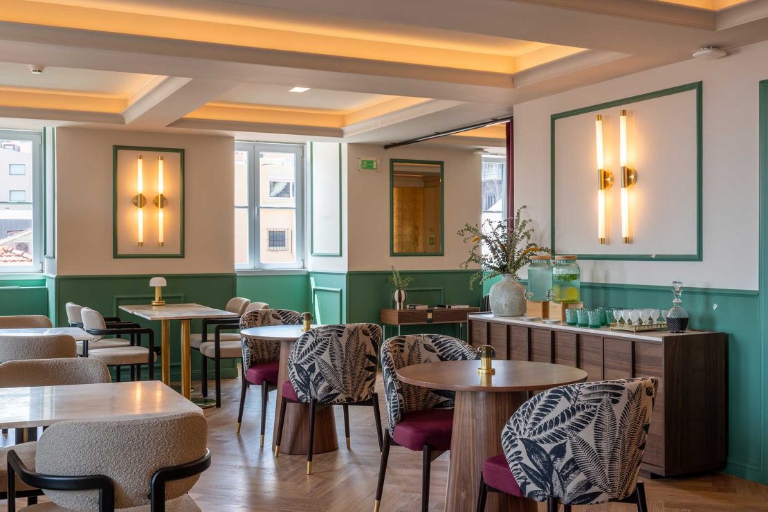 Bright cafe dining area with green wainscoting, marble tables, and patterned armchairs arranged for a meal service