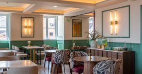 Bright cafe dining area with green wainscoting, marble tables, and patterned armchairs arranged for a meal service