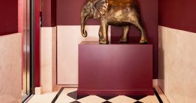 Bronze elephant statue on a burgundy pedestal in a red-walled foyer with a black-and-white checkered floor.