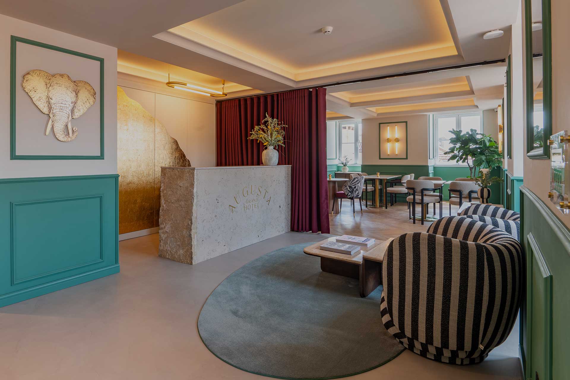 Hotel lobby with a stone reception desk, emerald green paneling, and a circular teal rug surrounding striped seating.