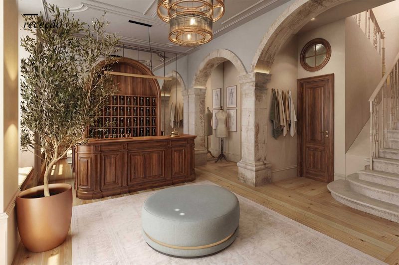 Elegant hotel reception area with a wooden curved desk, arches, and a large olive tree in a copper pot.