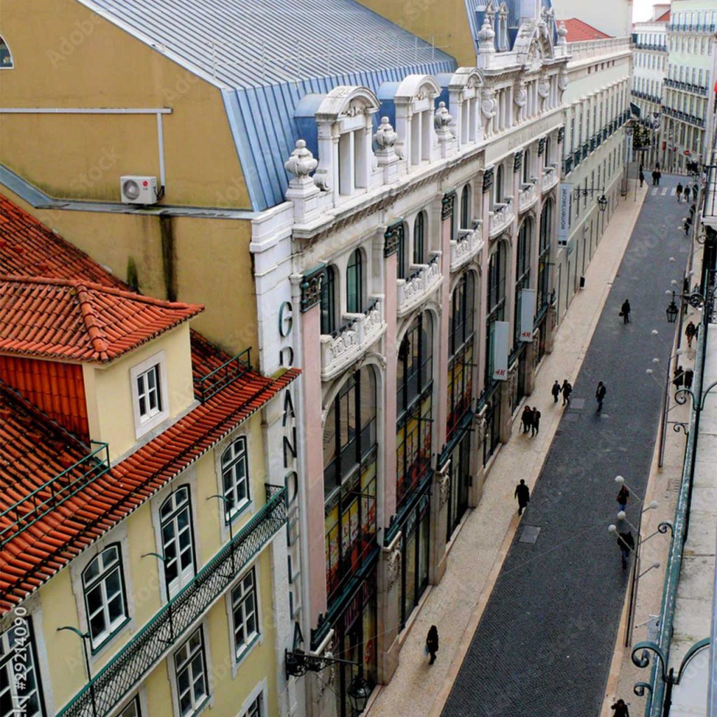 Narrow European street lined with ornate historic buildings, pedestrians walking along the sidewalk.