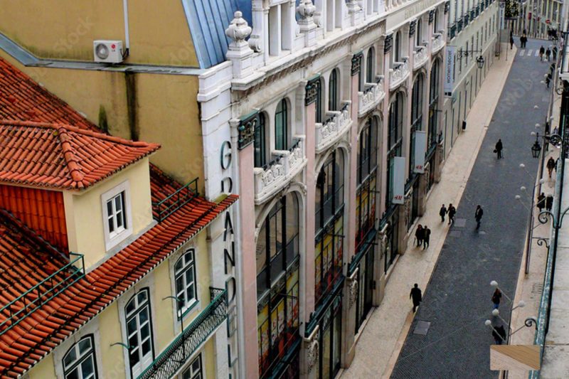 Sloped street in a European city, lined with pastel façades, arched windows, and red-tiled roofs.